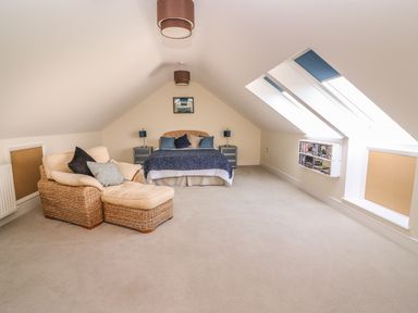 A bedroom with a bed and nightstands next to a wicker armchair under skylights at Cadwgan in Aberporth