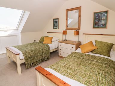 A bedroom with two single beds green throws and pillows a wooden dresser with lamps and a mirror at Cadwgan in Aberporth