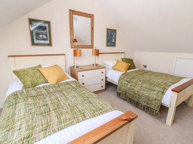 A bedroom with two single beds green and yellow pillows and blankets with a dresser and lamps in between at Cadwgan in Aberporth