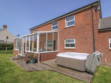 The exterior of a brick house with a wooden deck a hot tub a bench and a conservatory at Cadwgan in Aberporth