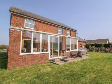 A brick house with a glass enclosed porch a bench and a lawn at Cadwgan in Aberporth