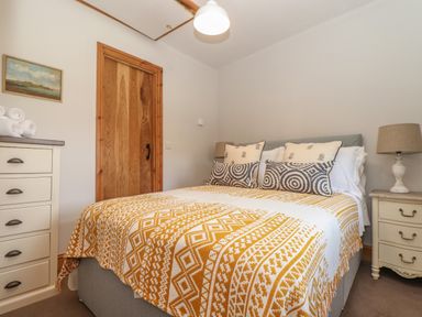 A bedroom with a double bed patterned blanket bedside tables lamps and a wooden door at Swallows Nest in Morvah