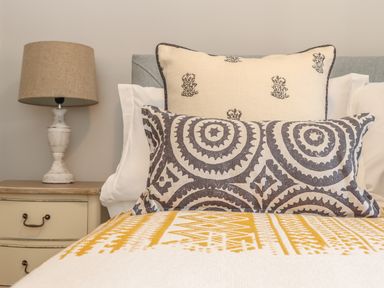 A bed with decorative pillows and a yellow patterned blanket next to a nightstand with a lamp at Swallows Nest in Morvah
