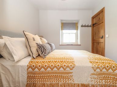 A bedroom with a patterned bedspread on a bed next to a window and a wooden door at Swallows Nest in Morvah