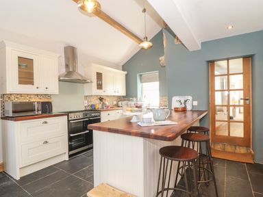 A kitchen with white cabinets a wooden countertop a stove and three bar stools at Swallows Nest Morvah