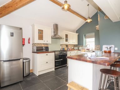 A kitchen with white cabinets wooden countertops and bar stools at Swallows Nest in Morvah