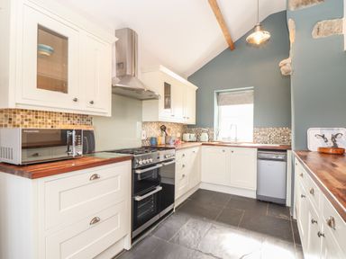A kitchen with white cabinets wooden countertops a black oven a microwave and a window at Swallows Nest in Morvah