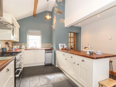 A kitchen with white cabinets wooden countertops a stove dishwasher and a kitchen island at Swallows Nest in Morvah