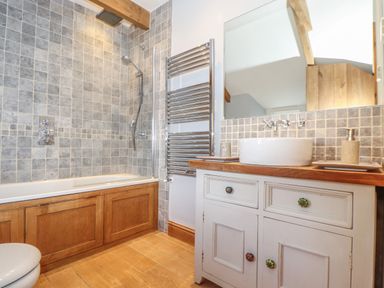 A bathroom with a bathtub shower area wooden paneling wooden floor and a white vanity with a round sink and mirror at Swallows Nest in Morvah