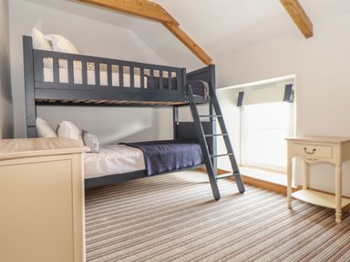 A bedroom with a black bunk bed a wooden chest of drawers a small cream bedside table and a window at Swallows Nest in Morvah