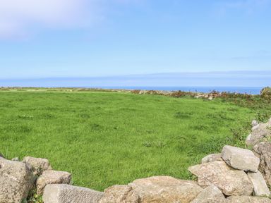 A grassy field bordered by stone walls and an ocean view at Swallows Nest in Morvah