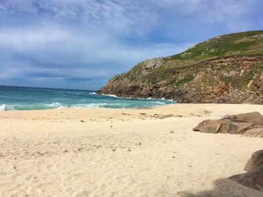 A sandy beach next to a rocky hill with ocean waves and a partly cloudy sky at Swallows Nest in Morvah