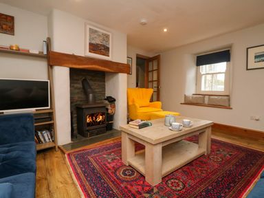 A living room with a fireplace a yellow armchair a wooden coffee table and a television at Swallows Nest in Morvah