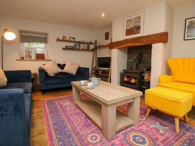 A living room with blue sofas a yellow armchair and a wooden coffee table on a patterned rug at Swallows Nest in Morvah