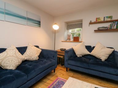 A living room with two blue sofas and beige pillows with a floor lamp and shelves with books at Swallows Nest in Morvah