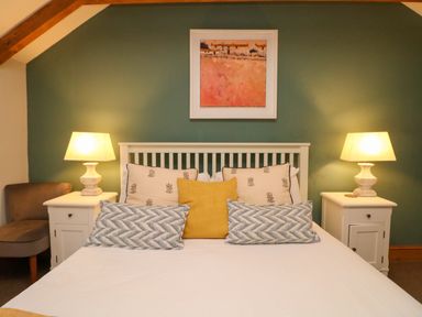 A bedroom with a white bed frame two white bedside tables with lamps a chair and a painting on a green wall at Swallows Nest in Morvah