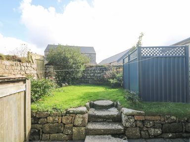 A small garden with stone steps and walls a wooden gate and blue fence panels at Swallows Nest in Morvah