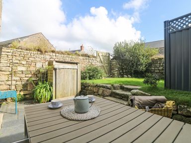 An outdoor patio with a table set with a teapot and cups a stone wall grass steps and a wooden gate at Swallows Nest in Morvah