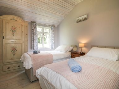 A bedroom with two beds a wooden wardrobe a window with floral curtains and a bedside table with a lamp at The Hen House in Stockwell Heath near Rugeley