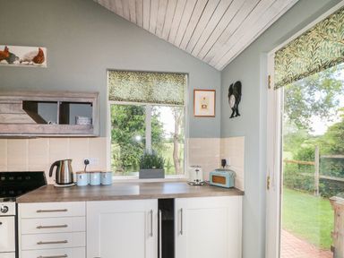 A kitchen with white cabinets a kettle toaster and radio on the counter and a window and door with patterned blinds at The Hen House in Stockwell Heath near Rugeley