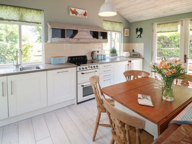 A kitchen with wooden dining table and chairs with flowers on the table at The Hen House in Stockwell Heath near Rugeley