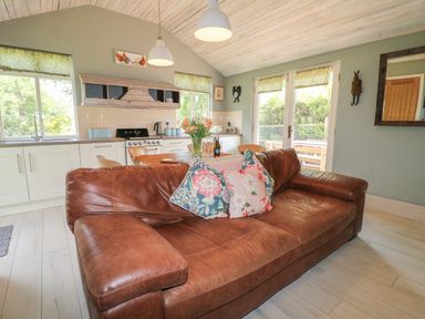 A kitchen and living area with a brown leather sofa and floral cushions at The Hen House in Stockwell Heath near Rugeley