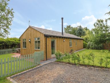 A wooden cabin with multiple windows surrounded by green lawn and a small green fence at The Hen House in Stockwell Heath near Rugeley