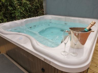 An outdoor hot tub with a bottle of champagne in an ice bucket and two empty glasses at The Hen House in Stockwell Heath near Rugeley