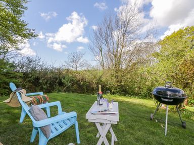 A garden with two blue chairs a small white table with a bottle and glasses and a barbecue grill at Orchard Loft Brownston near Modbury