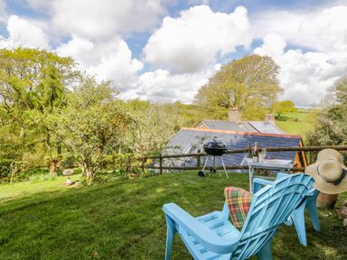 A garden with two blue chairs a small table a barbecue and trees at Orchard Loft in Brownston near Modbury