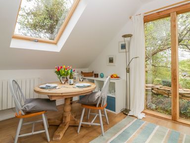 A small dining area with a round wooden table and two chairs under a skylight at Orchard Loft in Brownston near Modbury