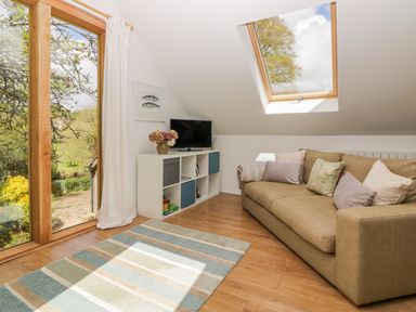 A room with a brown sofa with cushions a white cabinet with a TV a large window and a skylight at Orchard Loft in Brownston near Modbury