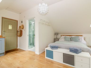 A bedroom with a bed pillows and folded towels a storage bench a nightstand lamp an open door revealing a shower and a closed door at Orchard Loft Brownston near Modbury
