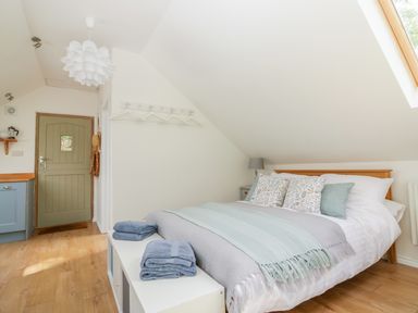 A bedroom with a bed pillows and blankets a small cabinet towels on a bench and a door at Orchard Loft Brownston near Modbury