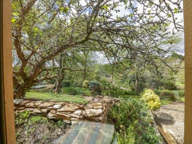 A garden with trees bushes flowers and a stone wall at Orchard Loft in Brownston near Modbury