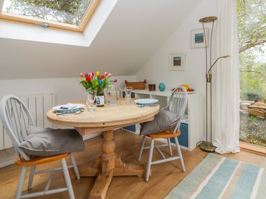 A dining area with a round wooden table set for two under a skylight at Orchard Loft in Brownston near Modbury