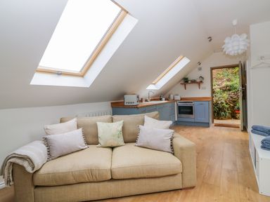 A loft living room with a sofa and kitchen cabinets under skylight windows at Orchard Loft in Brownston near Modbury