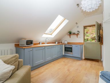 A kitchen with blue cabinets wooden countertops a skylight window an open door and a beige sofa at Orchard Loft in Brownston near Modbury