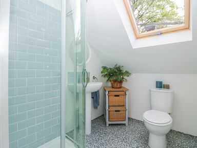 A bathroom with a shower, sink, toilet, wooden cabinet with wicker drawers and a skylight window at Orchard Loft in Brownston near Modbury