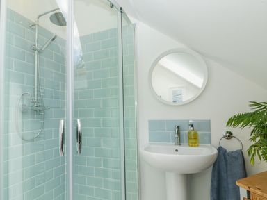 A bathroom with a shower enclosure with blue tiles a white pedestal sink a round mirror and a towel at Orchard Loft in Brownston near Modbury