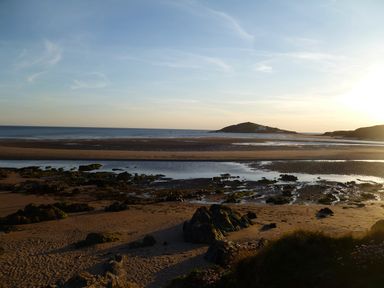 A beach with rocks and pools of water and an island in the distance at Orchard Loft Brownston near Modbury