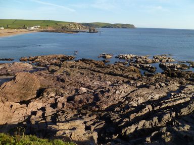 A rocky coastline with calm sea and grassy hills in the background at Orchard Loft in Brownston near Modbury