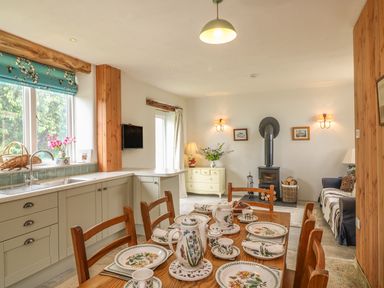 A kitchen dining area with a wooden table set with floral dishware a stove and a wooden cabinet at The Old Laundry in North Tawton