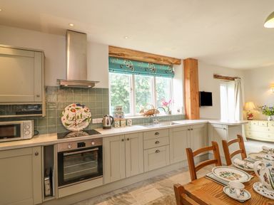 A kitchen with cabinets a stove a microwave a sink and a dining table with dishes at The Old Laundry in North Tawton