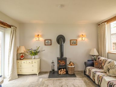 A living room with a wood burning stove flanked by sconces drawers with a lamp and flowers and a couch with cushions and a lamp at The Old Laundry in North Tawton