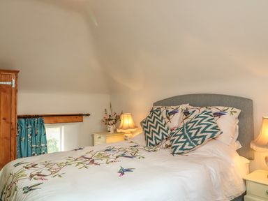 A bedroom with a bed featuring patterned bedding and pillows with bedside tables and lamps at The Old Laundry in North Tawton