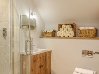 A bathroom with a glass shower door wooden cabinet under sink rolled towels and woven baskets at The Old Laundry in North Tawton