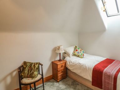 A small bedroom with a single bed a wooden chair a bedside table with a lamp and a window at The Old Laundry in North Tawton