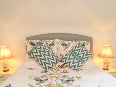 A bed with bird patterned bedding and chevron pillows with two table lamps on bedside tables at The Old Laundry in North Tawton