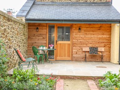 A small patio with green metal chairs a wooden bench with a cushion a table with tea set and flowers outside a wooden door at The Old Laundry in North Tawton